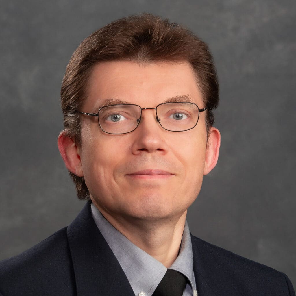 Headshot of Mikhail Dozmorov. He's wearing a light shirt with a black tie and suit jacket. He has short brown hair, light eyes and wire-framed glasses.