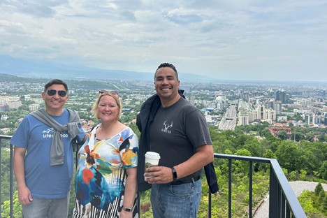 Drs. Chukmaitov, Swahn and Trevino stand smiling in front of a cityscape behind them.
