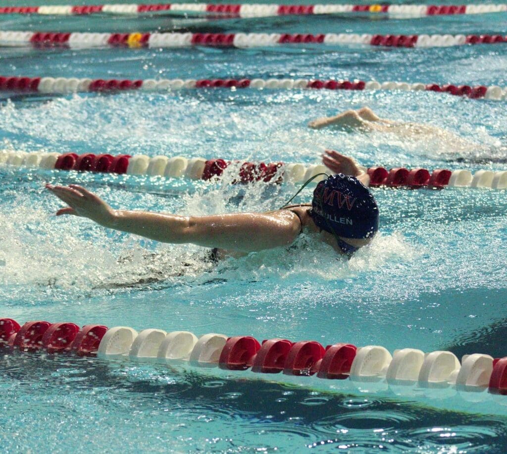 competitive swimmer is midstroke in a pool with white and red lanes 
