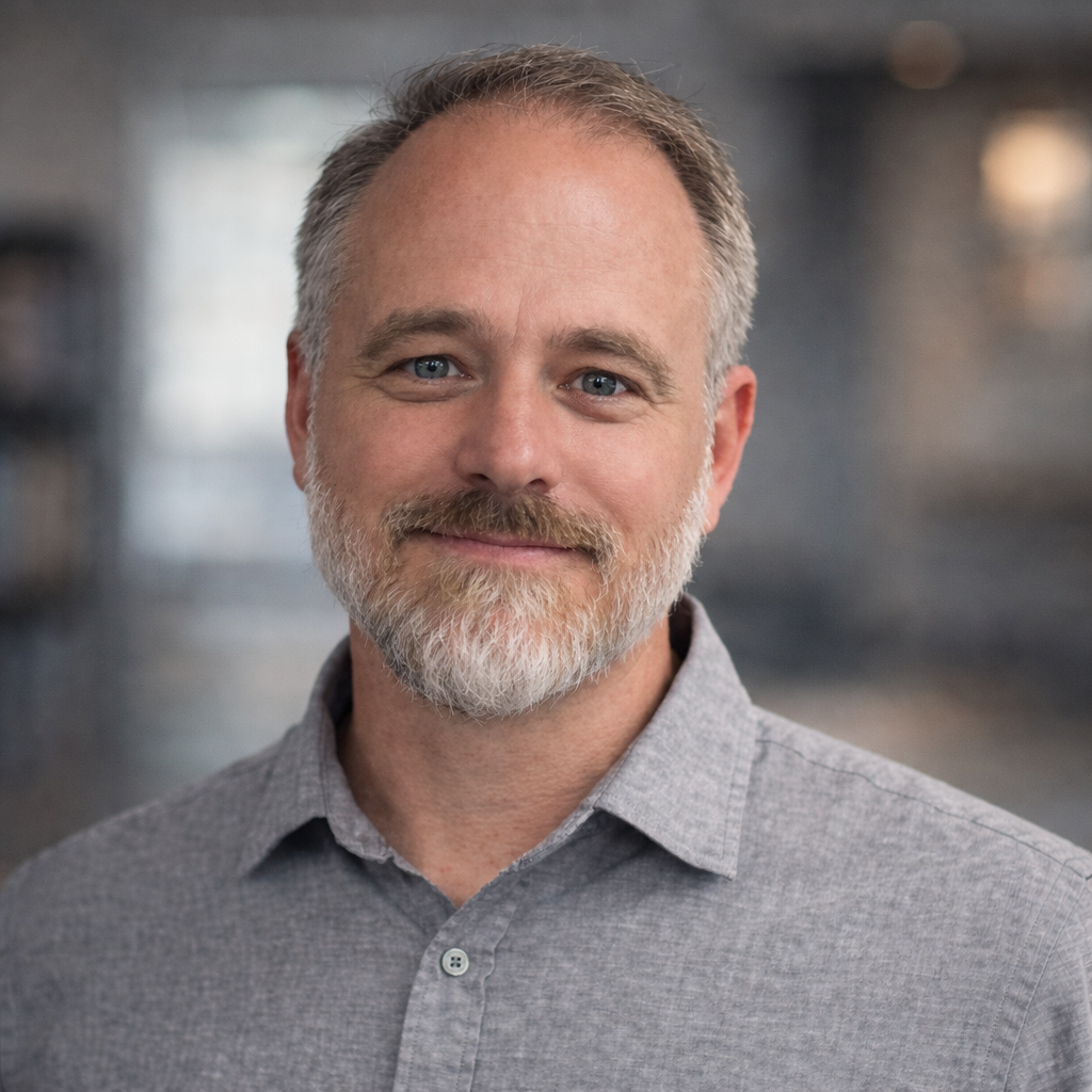 headshot of a smiling man with cropped graying hair, beard and mustache, wearing a gray collared shirt.