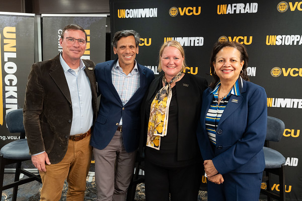 Four colleagues stand smiling in business attire and VCU branding behind them