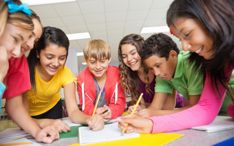 Image of young students gathered around schoolwork.