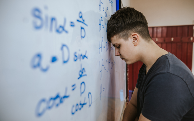 Picture of student leaning his head on a whiteboard with math equations