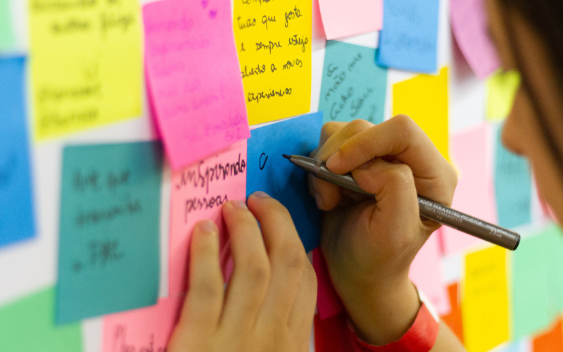 Image of a wall covered with colorful Post-its and a child writting on one.