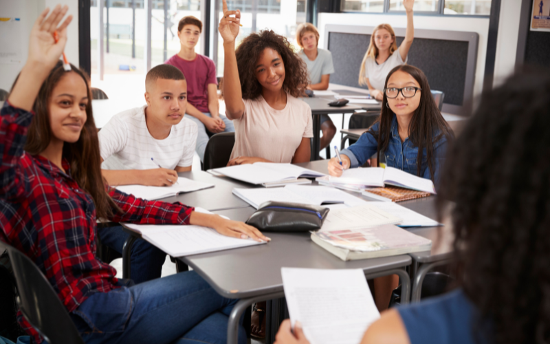 Image of students in highschool classroom, some are raising thier hands