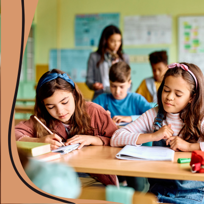 Image of elementary students working at the desks with the teacher in the background