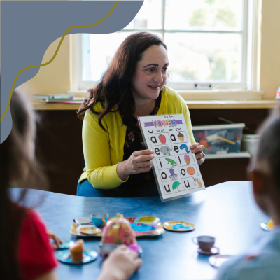 Photo of a teacher showing a picture of letters from the alphabet with corresponding images