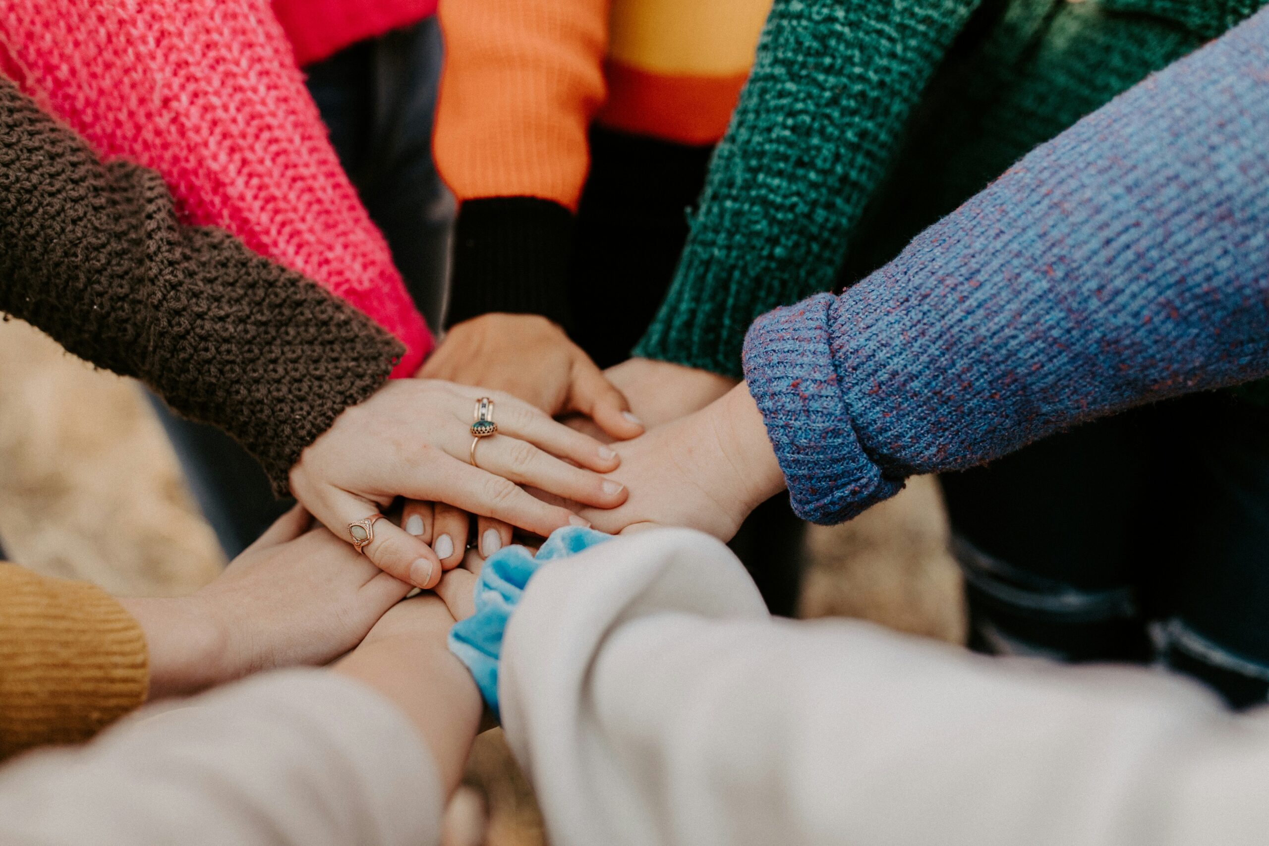 The arms of seven people reach into the center, their hands stack on top of one another